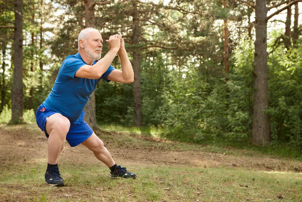 Portrait of healthy active elderly male doing side lunges
